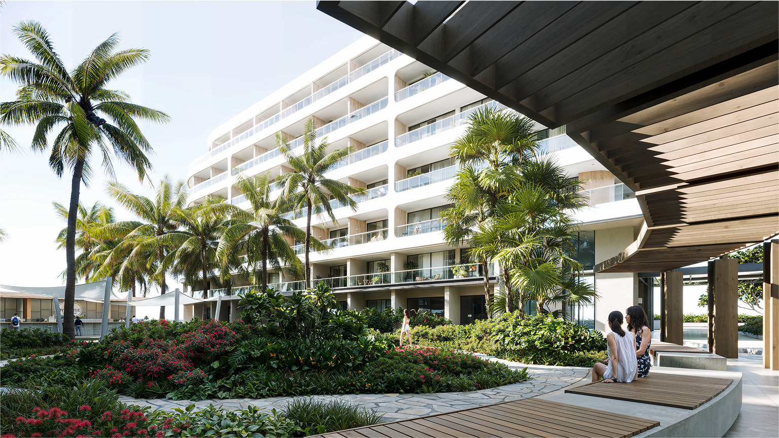 Two women relax on a bench in a lush Palm Beach courtyard, modern building in background.