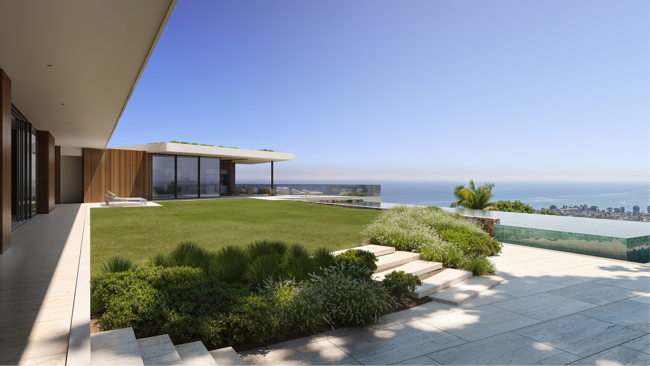 Modern luxury home overlooking ocean; grassy lawn, infinity pool, and stone steps.